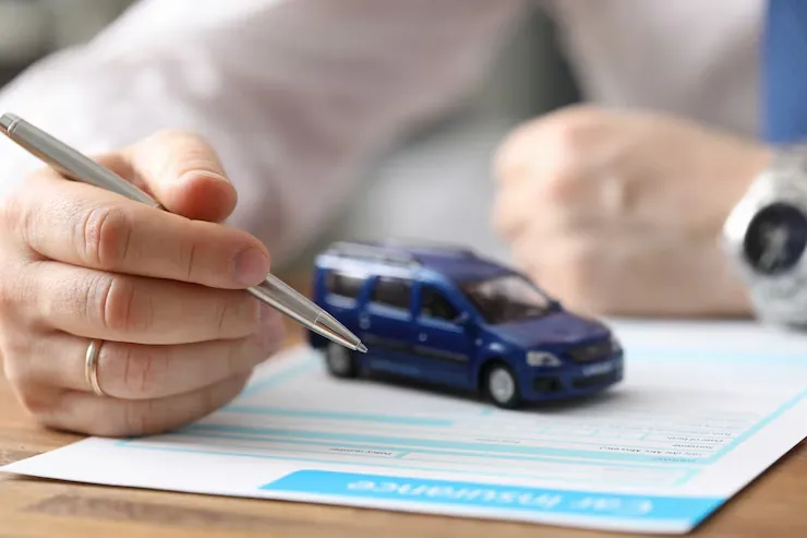 A close-up of a businessman holding a pen, signing a document next to a blue toy car on a desk A close-up of a businessman holding a pen, signing a document next to a blue toy car on a desk