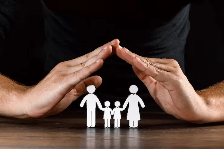 Two hands are cupped protectively over paper cutouts of a family a man, woman, and child, symbolizing care and protection Two hands are cupped protectively over paper cutouts of a family a man, woman, and child, symbolizing care and protection